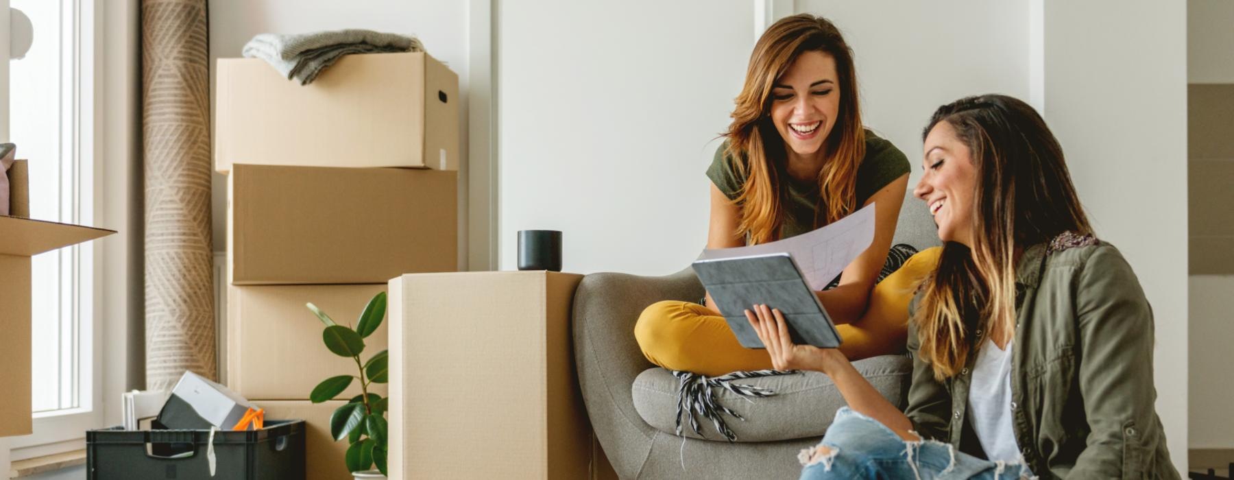 a person sitting on the floor with a friend sitting in a chair looking at a laptop