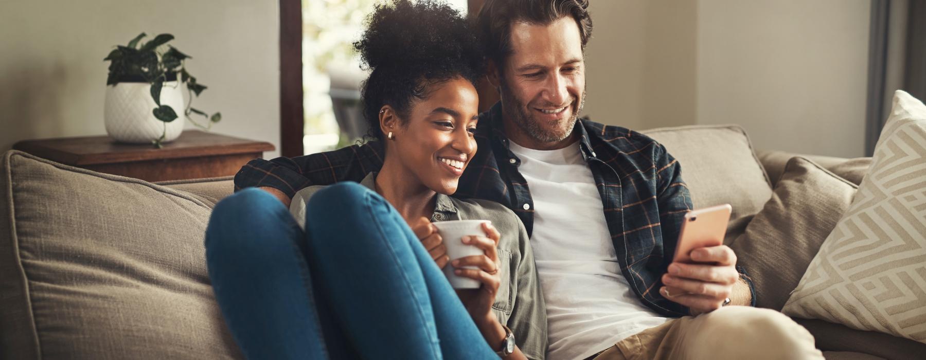 a man and woman sitting on a couch and looking at a cell phone